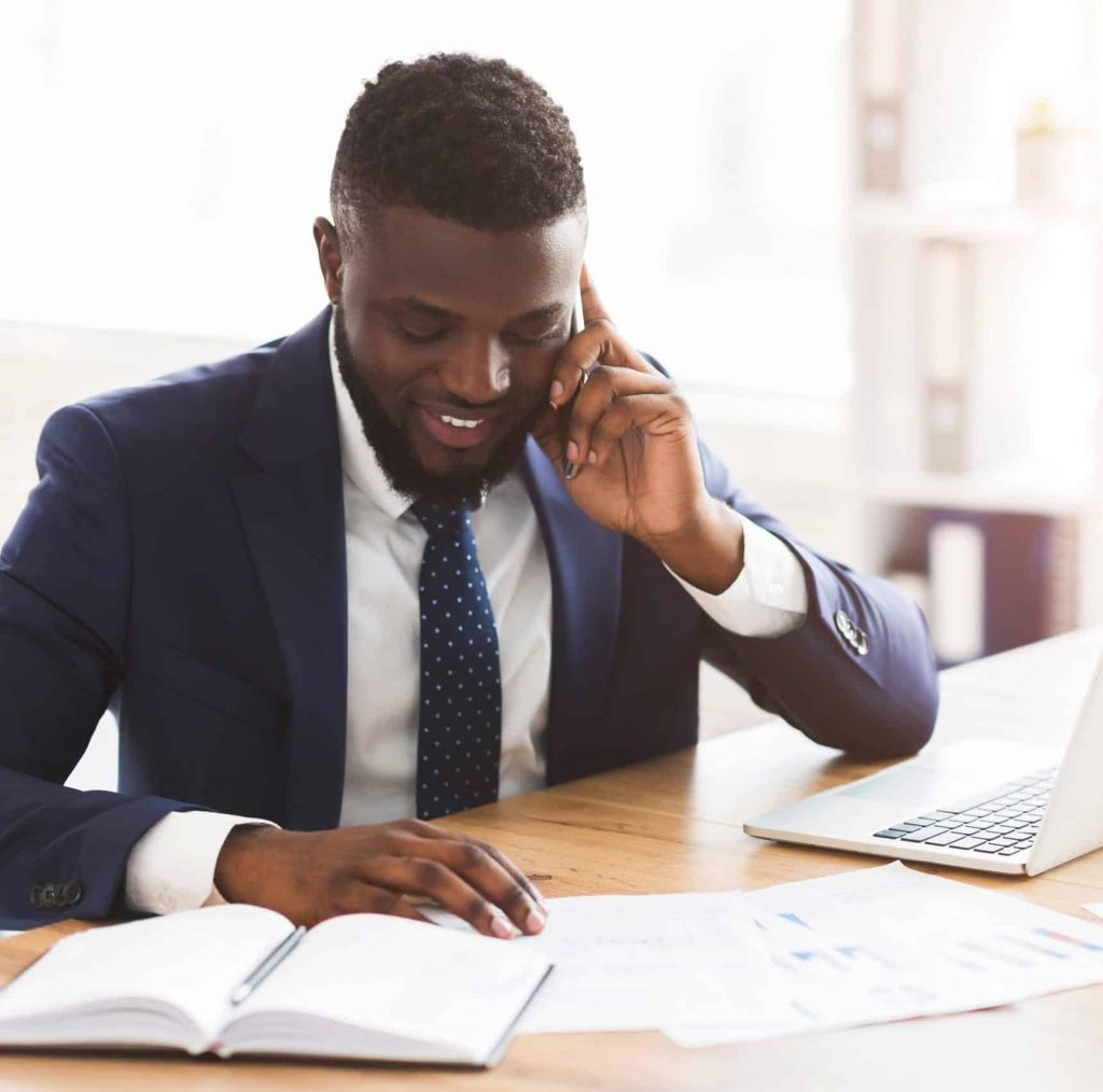 Smiling african american businessman checking marketing research in modern office, talking with assistant by smartphone, empty space